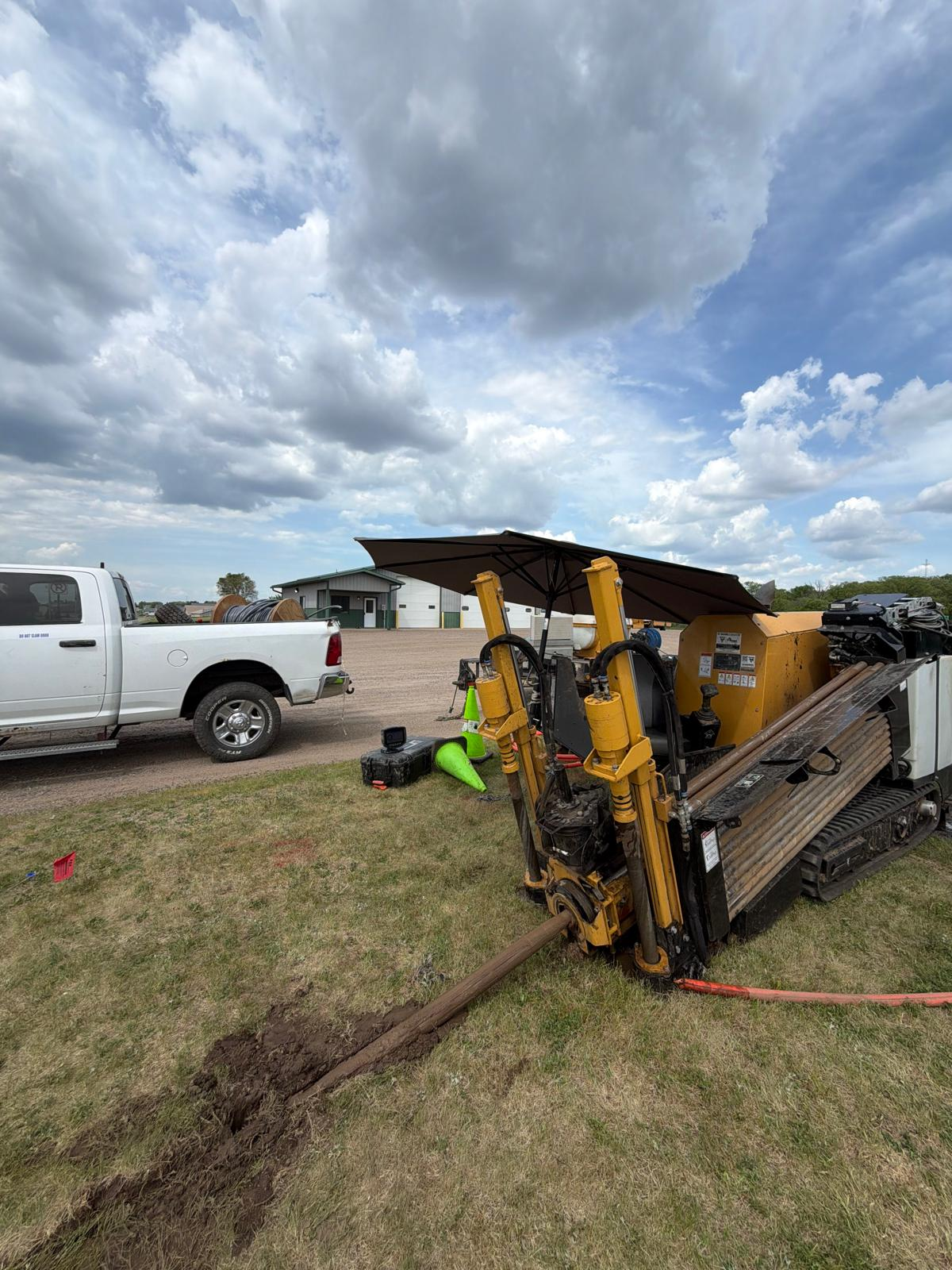Directional drill rig actively boring conduit next to service pickup truck on a rural jobsite