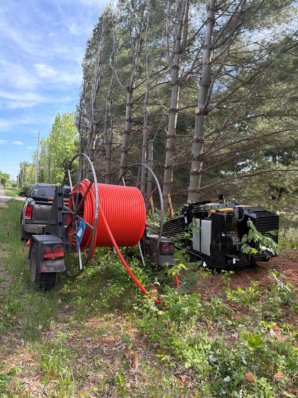 Fiber conduit reel trailer staged alongside directional drill rig on a tree-lined road